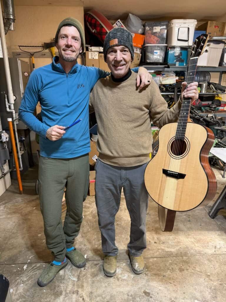 Two men in a workshop holding a Polaris acoustic guitar, smiling and posing for the photo.
